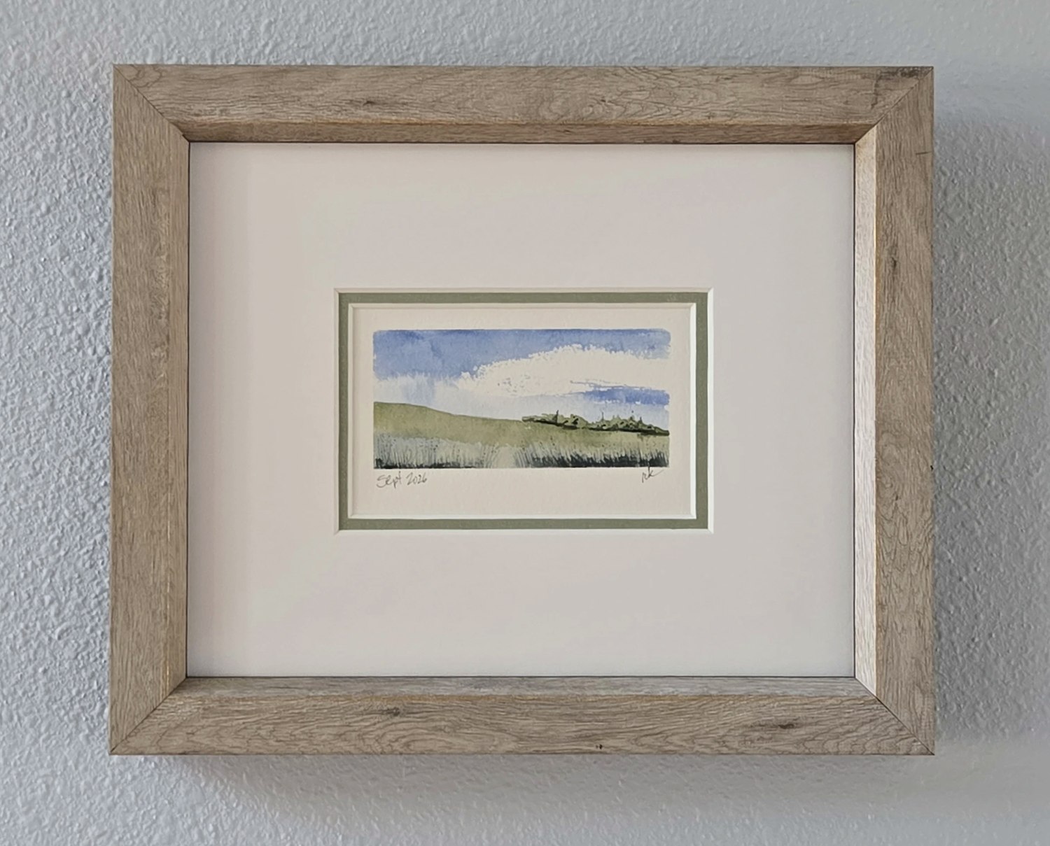 A framed hand-painted landscape card hanging on the wall at home