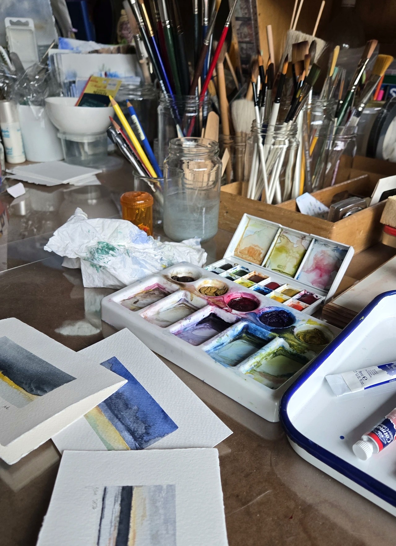 Richard's real working table — brush jars, well-used palettes, paint-stained rag and blue test strips